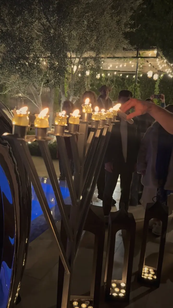 Miracle of Light 2025: lighting the lamps of the menorah by the pool, lanterns glowing below and guests gathered behind